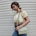 Stylish young curly woman with a yellow blouse top in blue classic jeans with a fashion bag walks near a siding wall on the street Royalty Free Stock Photo