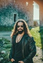 Stylish young fashionable man with long wavy hair wearing bikers leather jacket and sunglasses. Self confident handsome Royalty Free Stock Photo