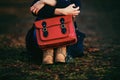 Stylish young girl in brown shoes and warm coat sits in the park with a red bag Royalty Free Stock Photo