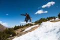 Stylish young girl snowboarder does the trick in jumping from a snow kicker against the blue sky clouds and mountains in