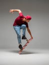 Stylish young guy skateboarder stands on skateboard in studio  on gray background. Skateboarding tricks Royalty Free Stock Photo