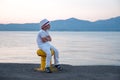 Kid in white clothes sitting by the ocean, sea with mountains on background. Sitting and waiting on seascape and Royalty Free Stock Photo