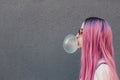 Stylish young hipster woman with long pink hair blowing a bubble with bubble gum. Royalty Free Stock Photo