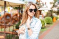 Stylish young hipster woman in trendy in sunglasses in fashionable blue summer denim jacket in vintage white lace blouse Royalty Free Stock Photo