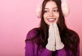 Graceful young lady in a knitted sweater and winter headphones and mittens on a pink background Royalty Free Stock Photo