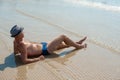 Stylish young male model man lying on beach sand wearing hipster summer hat enjoying summer travel holiday near the sea Royalty Free Stock Photo