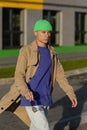 Stylish a young male model wearing green hat, brown jacket with light grey wall background on street Royalty Free Stock Photo