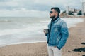 Stylish young man with a beard standing near ocean with a cup of tea Royalty Free Stock Photo