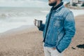 Stylish young man with a beard standing near ocean with a cup of tea Royalty Free Stock Photo