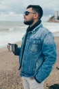 Stylish young man with a beard standing near ocean with a cup of tea Royalty Free Stock Photo