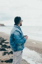 Stylish young man with a beard standing near ocean with a cup of tea Royalty Free Stock Photo