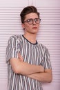 Stylish young man hipster in fashionable glasses with a hairstyle in a trendy striped t-shirt posing near a vintage wooden pink