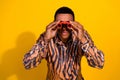 Young man looking through binoculars against a vibrant yellow background, wearing a tiger print shirt and expressing Royalty Free Stock Photo