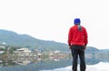 Stylish young man in red coat standing on the pier by the lake in the park at autumn. male enjoying view over the lake at cloudy Royalty Free Stock Photo