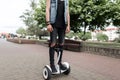 Stylish young man in ripped black jeans in a denim vest in a t-shirt in trendy sneakers stands a hoverboard in the street