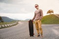 A stylish young man standing along a winding mountain road with a skate or longboard in his hands the evening after Royalty Free Stock Photo