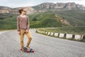 A stylish young man standing along a winding mountain road with a skate or longboard in his hands the evening after Royalty Free Stock Photo