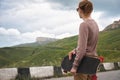 A stylish young man standing along a winding mountain road with a skate or longboard in his hands the evening after Royalty Free Stock Photo