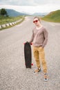 A stylish young man standing along a winding mountain road with a skate or longboard in his hands the evening after Royalty Free Stock Photo