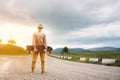 A stylish young man standing along a winding mountain road with a skate or longboard in his hands the evening after Royalty Free Stock Photo