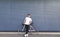 Stylish young man stands with a white highway bike on the background of the wall and looks at the camera