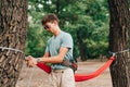 Stylish young man ties a hammock in the woods to a tree, ties the slings with his hands. The process of tying a hammock in the