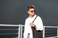 Stylish young man in trendy white shirt in fashionable sunglasses in vintage blue jeans with a cloth black bag Royalty Free Stock Photo