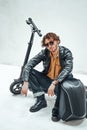 Stylish young man wearing sunglasses posing in the bright studio while sitting on the scooter with a backpack Royalty Free Stock Photo