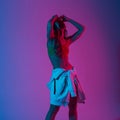 Stylish young model woman in fashionable clothes with a hoodie stands in a room with bright neon lights. Modern trendy girl posing Royalty Free Stock Photo