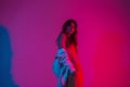 Stylish young model woman in fashionable clothes with a hoodie stands in a room with bright neon lights. Modern trendy girl posing Royalty Free Stock Photo