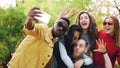 Stylish young people girls and guys are using smartphone to take selfie in park posing for camera and laughing. Students