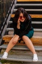 Stylish young pretty hipster woman sitting on iron house stairs, Happy beautiful girl in casual clothes green dress, black jacket Royalty Free Stock Photo