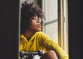 Stylish young sensual black pensive woman sitting near the window with a skateboard