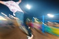 Stylish young skater in a fashionably tucked hat rides a skatepark at night. Night photo with the movement of lights and