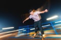 Stylish young skater in a fashionably tucked hat rides a skatepark at night. Night photo with the movement of lights and