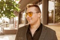 Stylish young smiling guy businessman of Caucasian appearance portrait in sunglasses, jacket and shirt on the street outdoor Royalty Free Stock Photo