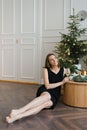 Stylish young woman in a black dress is relaxing with a glass of wine at the Christmas tree Royalty Free Stock Photo