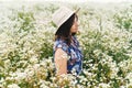 Stylish young woman in blue vintage dress and hat posing in summer meadow in many white wildflowers. Tranquil summer in