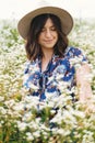 Stylish young woman in blue vintage dress and hat smiling in summer meadow in many white wildflowers. Tranquil summer in
