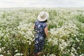 Stylish young woman in blue vintage dress and hat walking in summer meadow in many white wildflowers. Tranquil summer in