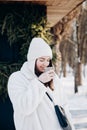 Stylish young woman with a cup of hot drink near a cafe in winter. Royalty Free Stock Photo