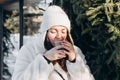 Stylish young woman with a cup of hot drink near a cafe in winter. Royalty Free Stock Photo