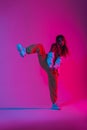 Stylish young woman dancer with trendy sports youth clothes in fashion sneakers stands on one leg in the studio with a bright pink