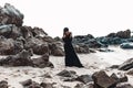 Stylish young woman in elegant black dress on the stone beach