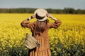 Stylish young woman in a field of yellow flowers. Girl in straw hat and in a floral dress and with a wicker bag Royalty Free Stock Photo