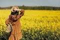 Stylish young woman in a field of yellow flowers. Girl in straw hat and in a floral dress and with a wicker bag Royalty Free Stock Photo