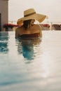 Stylish young woman in hat relaxing in pool and enjoying warm sunny light on summer vacation. Girl in sunhat on vacation in luxury Royalty Free Stock Photo