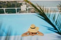 Stylish young woman in hat relaxing in pool under palm leaves and enjoying summer holiday. Summer vacation. Girl in sunhat on Royalty Free Stock Photo