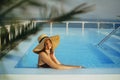 Stylish young woman in hat relaxing in pool under palm leaves and enjoying warm sunny light on summer vacation. Girl in sunhat on Royalty Free Stock Photo