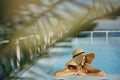 Stylish young woman in hat relaxing in pool under palm leaves and enjoying warm sunny light on summer vacation. Girl in sunhat on Royalty Free Stock Photo